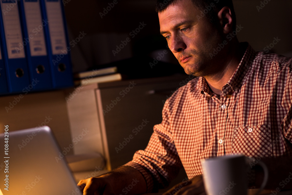 Young businessman working late on laptop at night in dark office Young businessman working late on laptop at night in dark office