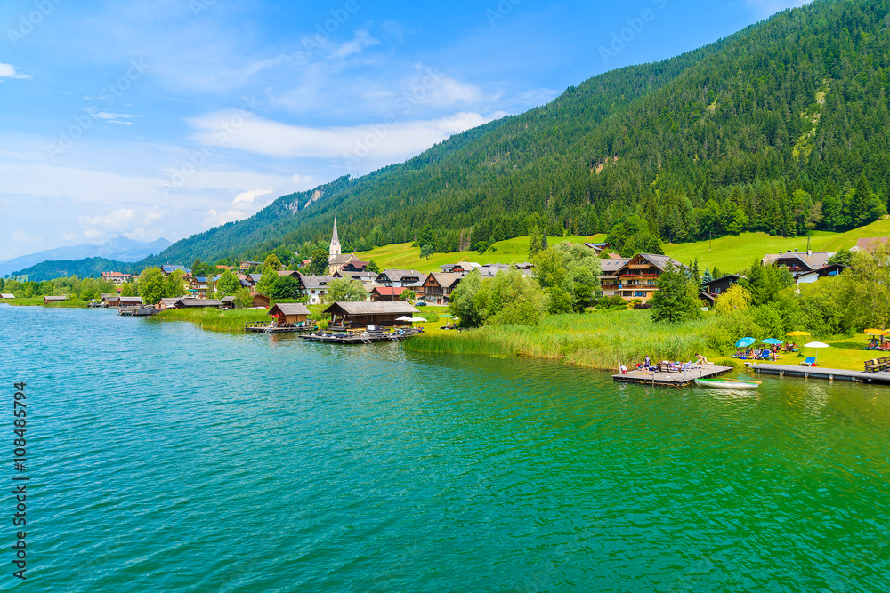 A view of beautiful green water Weissensee alpine lake and village in summer landscape of Alps Mountains, Austria