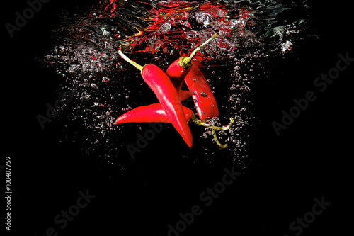 Several red peppers fallen into the water isolated on the black background