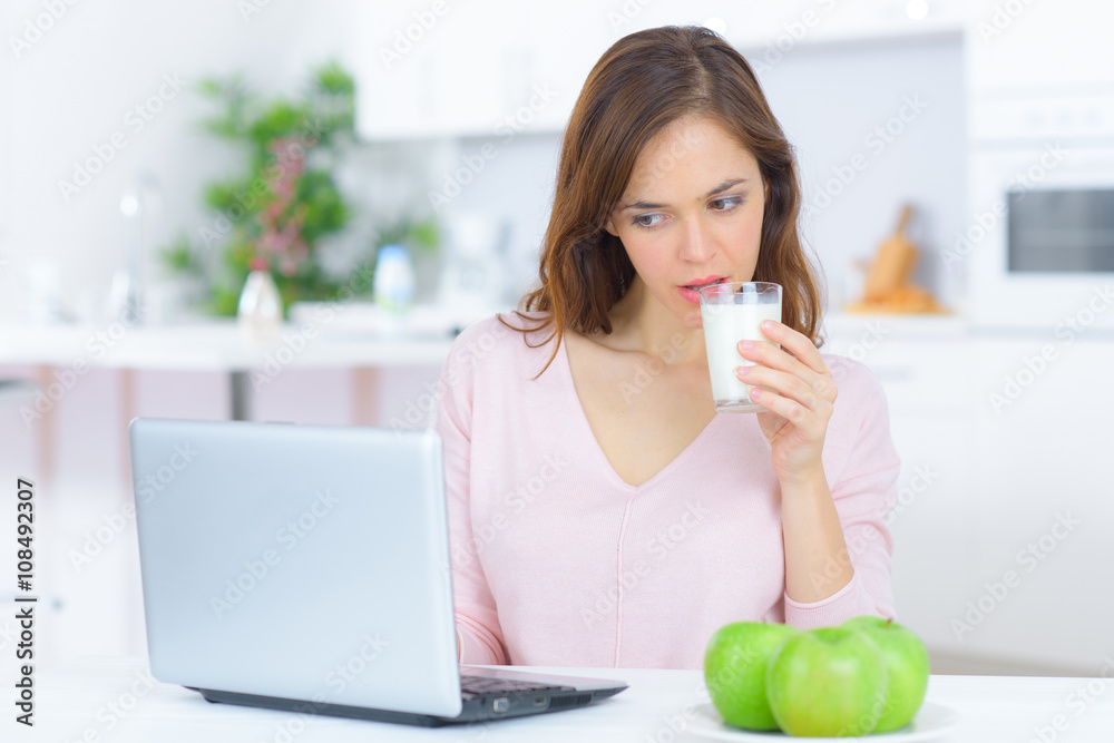 Lady drinking glass of milk, looking at laptop Lady drinking glass of milk, looking at laptop