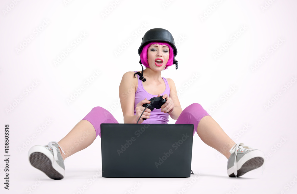 Young girl in the helmet with joystick sits on the floor and playing game on a laptop Young girl in the helmet with joystick sits on the floor and playing game on a laptop