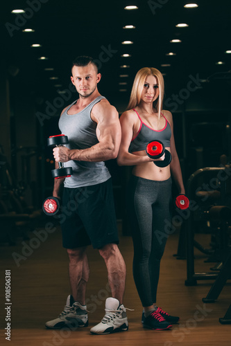 beautiful young sporty sexy couple showing muscle and workout in gym dumbbell