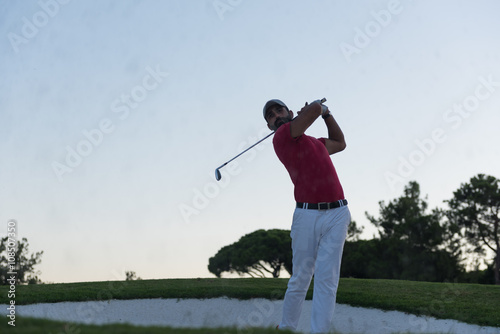 golfer hitting a sand bunker shot on sunset