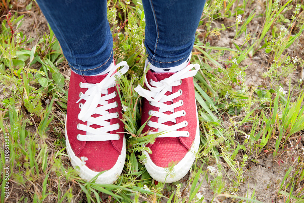 With red sneakers and jeans treading the grass