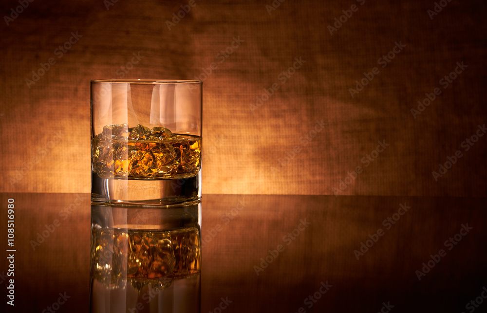 A glass of whisky on a reflective bar top surface with edge highlights.