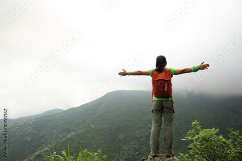cheering young asian woman open arms on mountain peak rock