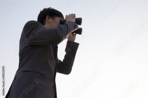 Asian businessman using binoculars during sunset being isolated