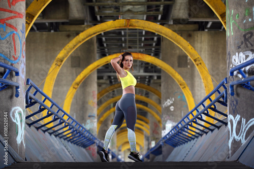 Sexy fitness girl standing on a bridge with graffiti