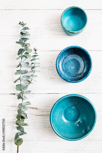 Three different  turquoise empty ceramic empty plates and evergreen branch on a white wooden background. Top view on set of trendy empty plates. Organic food, healthy life, pottery, decoration concept