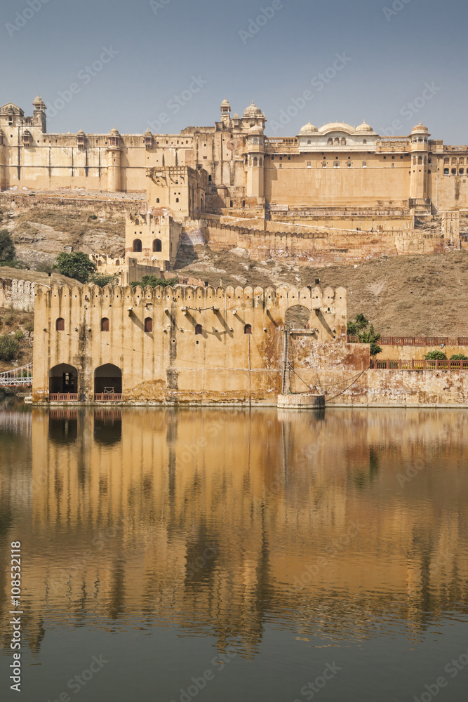 The Amber Fort in Jaipur, Rajasthan, India with the Moata Lake in the foreground, against a blue sky
