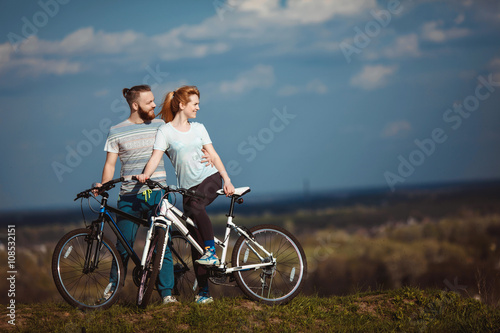 Beautiful young couple in love walking with bicycles hugging and looking towards the beautiful nature and the blue sky. The concept of active rest