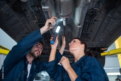 Mechanics examining car using flashlight