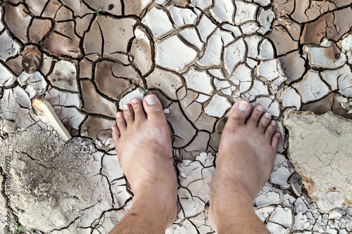 Barefoot standing on dry and cracked ground, conservation concept, dramatic style