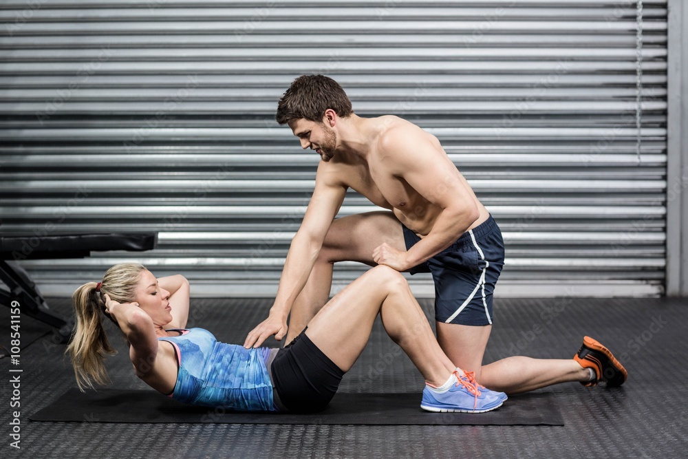Fototapeta premium Male trainer assisting woman with sit ups
