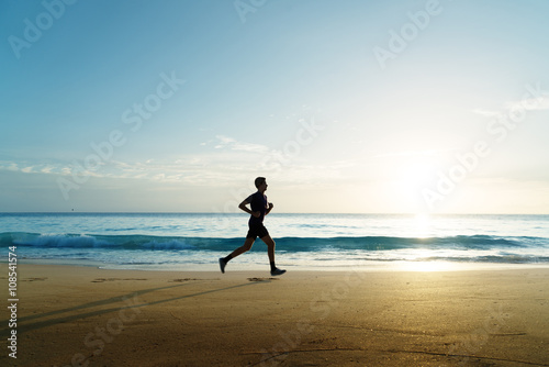 Man running on tropical beach at sunset