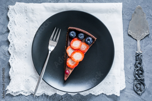 Piece of chocolate pie (cake, tart) decorated with fresh fruits and berries on black plate. Top view photo