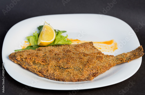 Whole roasted fish served with herbs, lemon on white plate