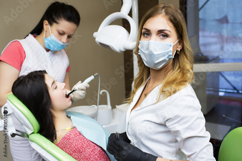 Portrait of beautiful dentist at office. Doctor and patient in background