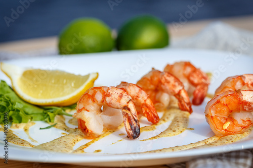 Grilled prawns with sauce and lemon on white plate.