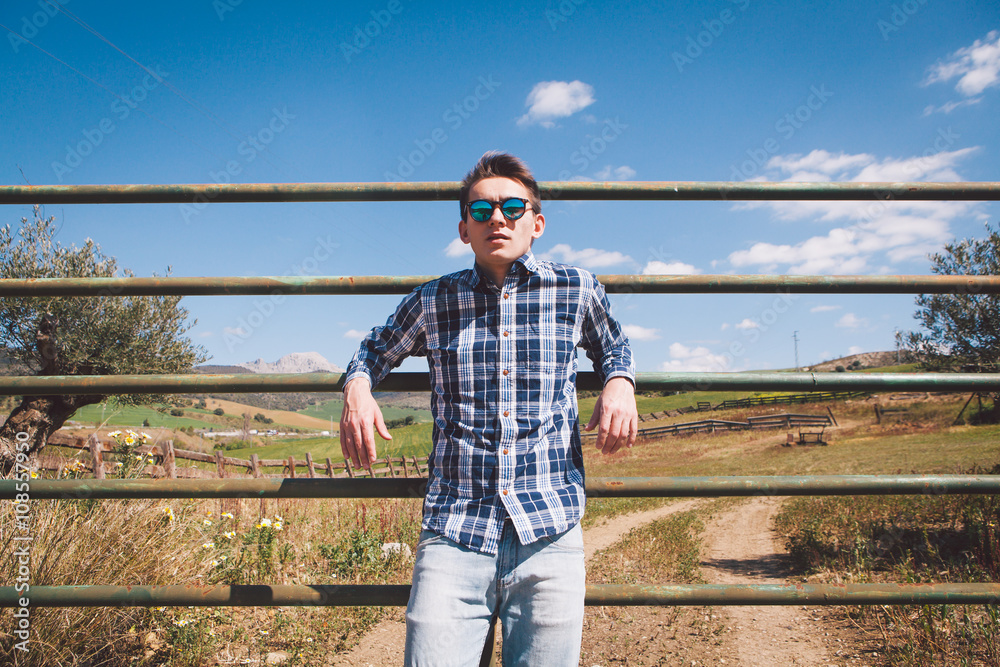 Young man posing in a farm fence at the countryside.