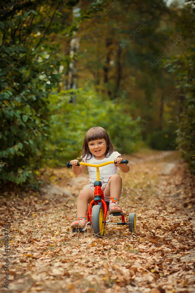 Adorable girl riding a bike on beautiful autumn day. childhood, leisure, friendship and people concept. walks in the woods on a sunny autumn day. Children playing outdoors. Happy family. series Adorable girl riding a bike on beautiful autumn day. childhood, leisure, friendship and people concept. walks in the woods on a sunny autumn day. Children playing outdoors. Happy family. series