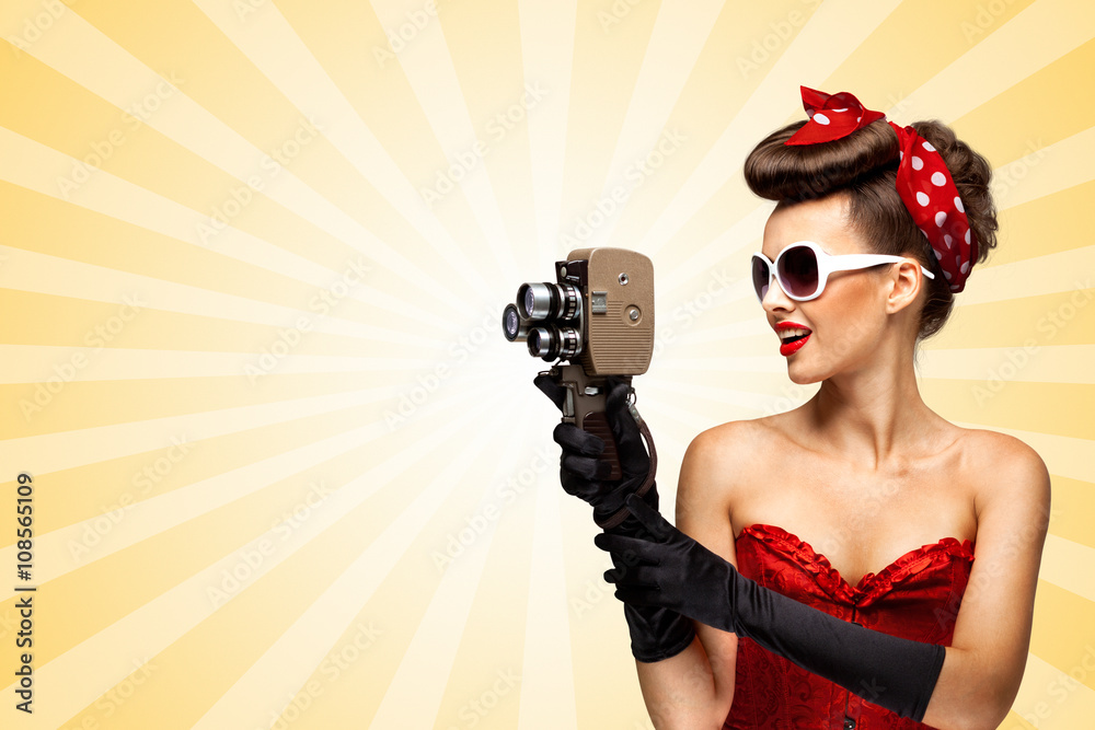 Shooting old movie / Retro photo of a glamorous pin-up girl with an old vintage cinema 8 mm camera shooting a movie on colorful abstract cartoon style background. Shooting old movie / Retro photo of a glamorous pin-up girl with an old vintage cinema 8 mm camera shooting a movie on colorful abstract cartoon style background.