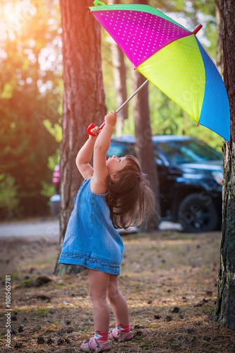 Little girl in jeans dress playing in a pine forest with color umbrella. soft light effect. childhood, leisure, friendship and people concept. Sunny summer day. Happy family. series
