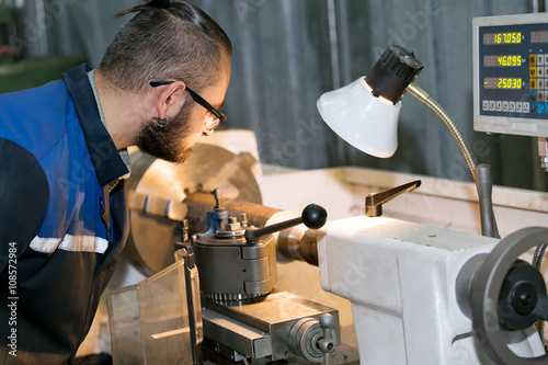 metalworking industry: machinery repairman worker processing metal piece at lathe machine in factory workshop photo
