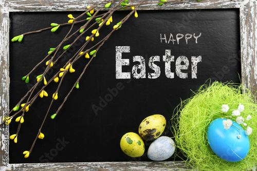 Easter greeting card. Colorful eggs with branches on blackboard, top view