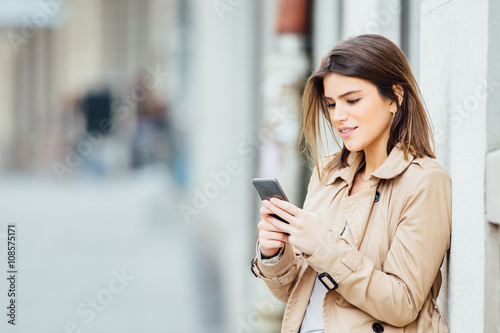 Beautiful young woman standing at the street and using her mobile phone