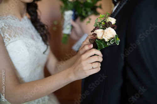 a brides hand putting the boutonniere flower on a groom