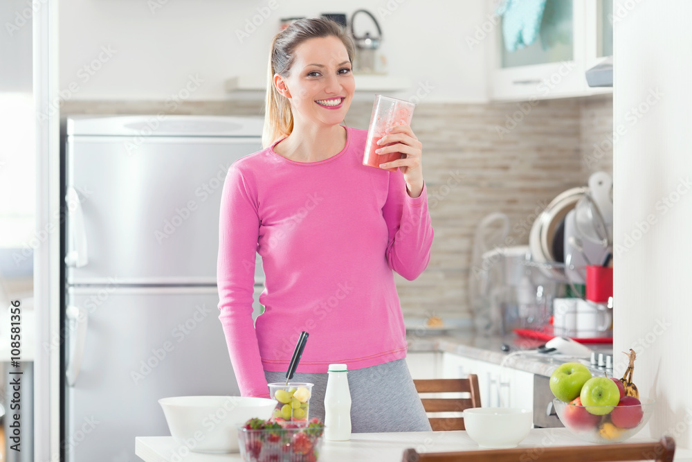 Portrait of beautiful young woman drinking strawberry smoothie in her kitchen Portrait of beautiful young woman drinking strawberry smoothie in her kitchen