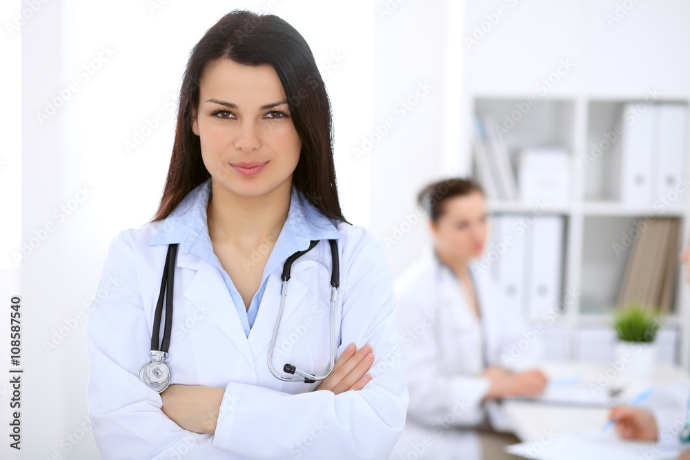 Brunette female doctor on the background of colleagues talking to each other in hospital Brunette female doctor on the background of colleagues talking to each other in hospital