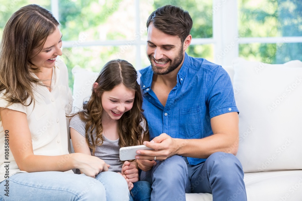Family looking at smart phone while sitting on sofa Family looking at smart phone while sitting on sofa