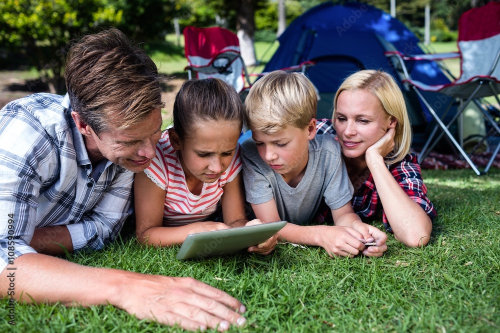 Fototapeta premium Family lying on grass and using digital tablet