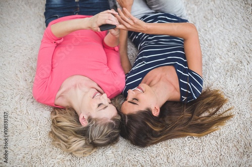 Two beautiful women lying on rug looking at the mobile phone
