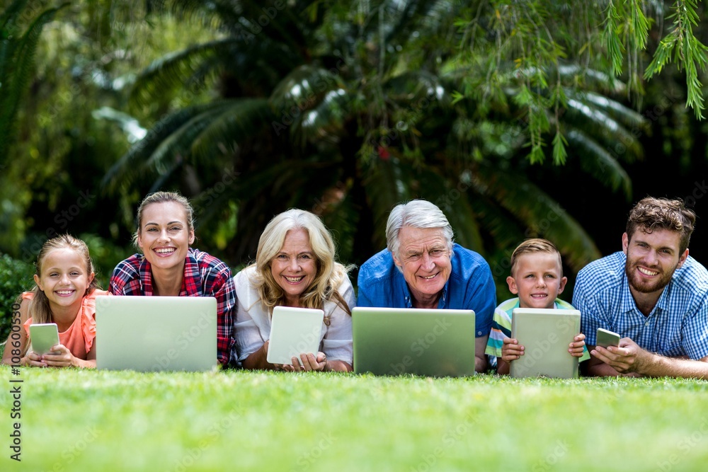 Portrait of family with technologies lying at yard 