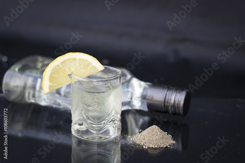 A glass of vodka with ice and lemon on a black background, black ground pepper