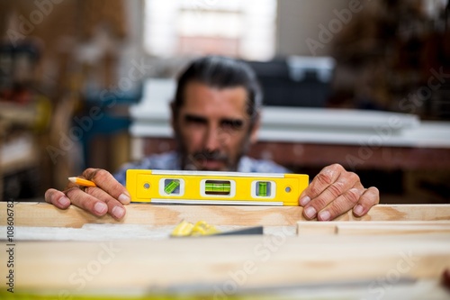 Carpenter measuring a length of wooden plank with spirit level