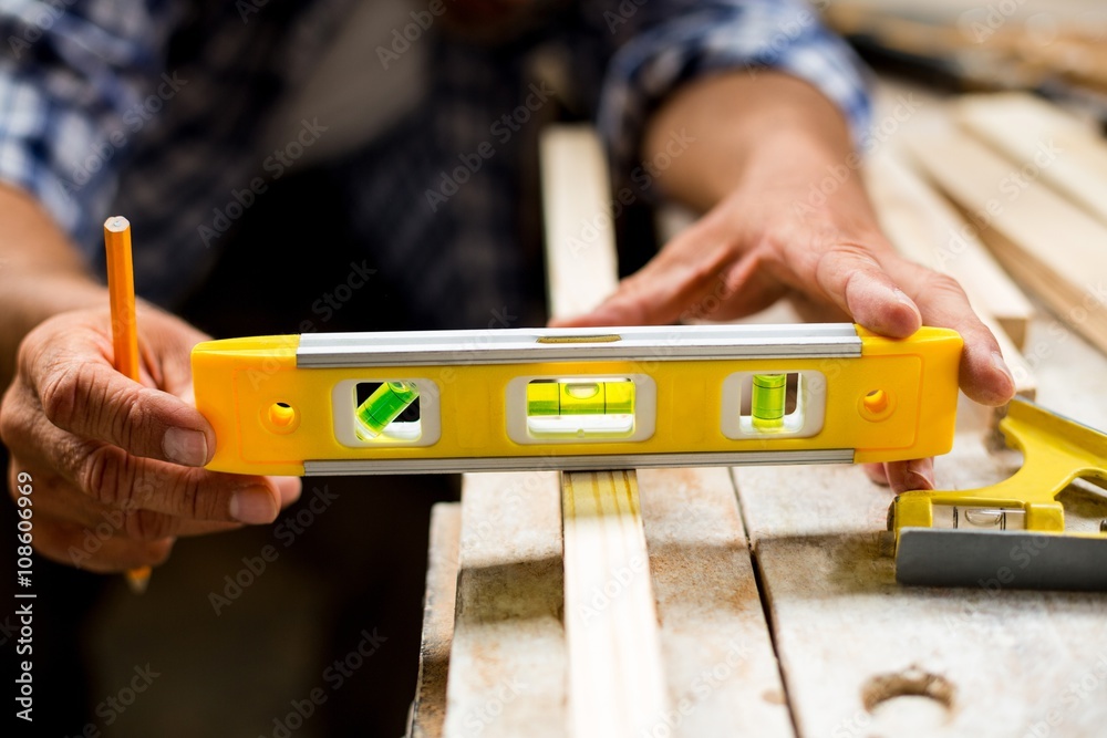 © Wavebreak Media - Carpenter measuring a length of wooden plank with spirit level