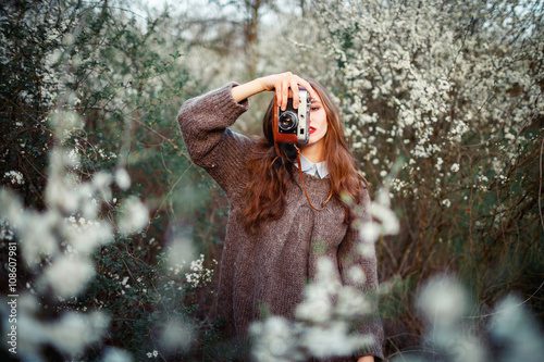 young beautiful girl with long hair brown hair, expressive cheekbones free warm sweater and pants with a film camera in hand walks on spring park