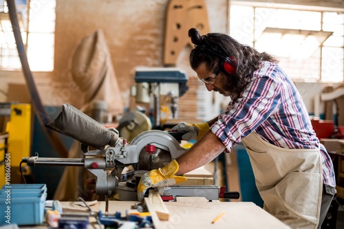 Carpenter cutting wooden plank with circular saw in workshop
