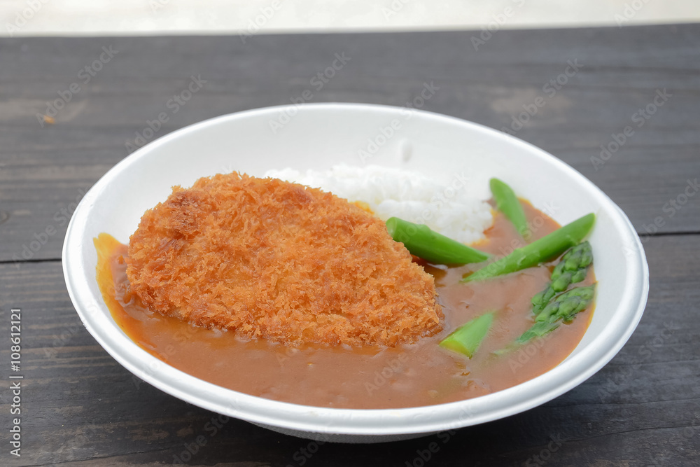 Curry rice with fried pork and asparagus on white plate on wood table Curry rice with fried pork and asparagus on white plate on wood table