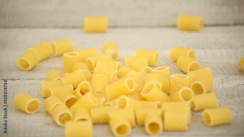 Hands pouring Mezze Maniche pasta onto wood Hands pouring Mezze Maniche pasta onto wood