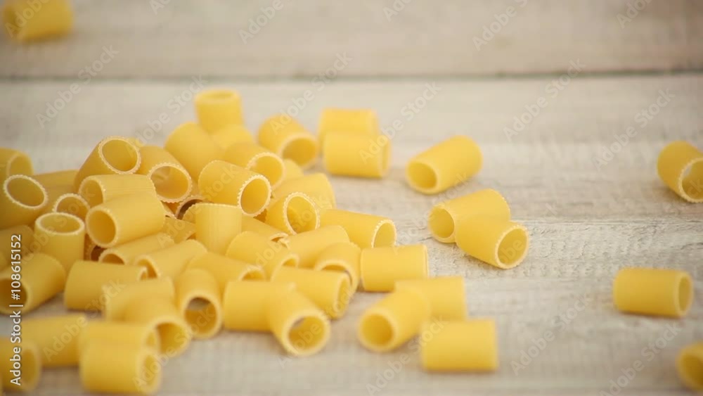Hands pouring Mezze Maniche pasta onto wood with copy space Hands pouring Mezze Maniche pasta onto wood with copy space