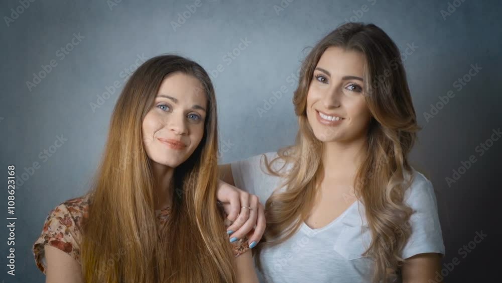Portrait of two beautiful girls smiling and looking at camera in studio. Portrait of two attractive caucasian smiling women isolated on grey background. Portrait of two beautiful girls smiling and looking at camera in studio. Portrait of two attractive caucasian smiling women isolated on grey background.