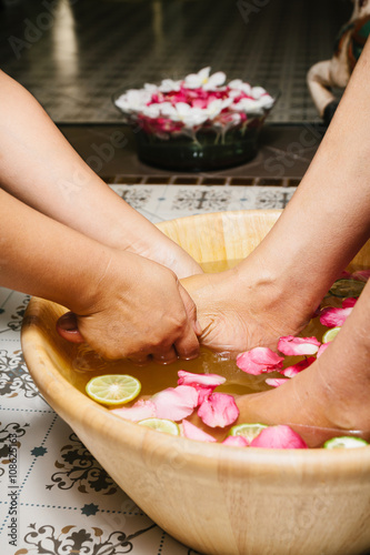 Closeup shot of a woman feet dipped in water with petals in a wooden bowl. Beautiful female feet at spa salon on pedicure procedure. Shallow depth of field with focus on feet. 