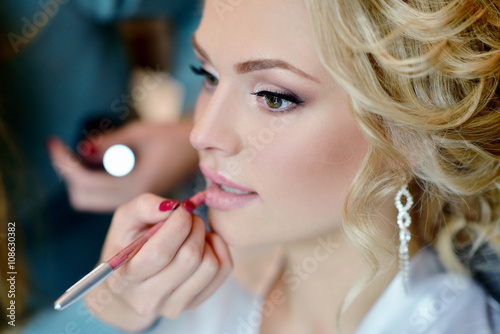 Wedding makeup artist making a make up for bride. Beautiful sexy model girl indoors. Beauty woman with curly hair. Female portrait. Bridal morning of a cute lady. Close-up hands near face