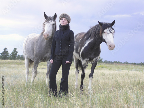 A young woman standing with two Spanish Mustang mares out in the pasture