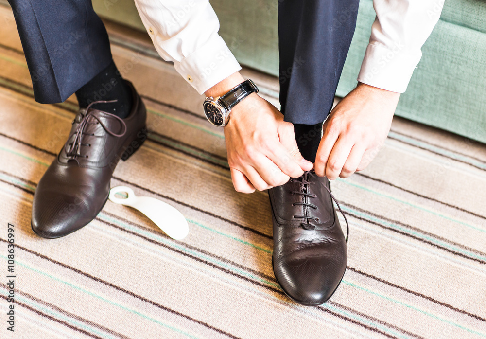 Close-up young man tying elegant shoes indoors